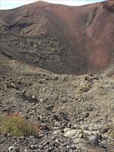 Close-up of a rocky crater with red volcanic soil and sparse vegetation, barren landscape with