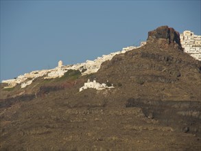 Steep cliffs of Santorini, strewn with the characteristic whitewashed houses under a clear sky,