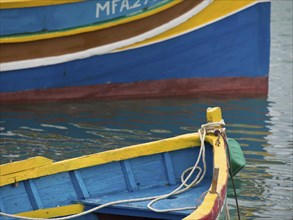 A blue and yellow fishing boat lies calmly in the water of the harbour, many colourful fishing