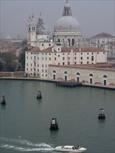 Venetian buildings with domes on the water, a small boat in a misty atmosphere, church towers and