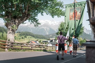 People in traditional traditional costume carry a banner through an Alpine village in sunny weather