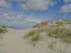 Sandy path through dune landscape with grass under cloudy sky, dune with dune grass and a boat by