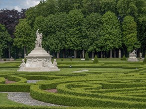 Spacious baroque garden with symmetrical hedges and several sculptures, surrounded by trees, park