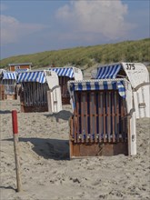 Beach with beach chairs in front of dunes and partly cloudy sky, dunes and beach at the sea with