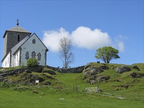 White church with stone tower on a rocky hill, tree and blue sky, old stone church and many