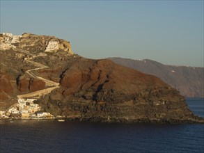 A coastline of Santorini with steep cliffs and houses rising above the azure blue sea, rocky island