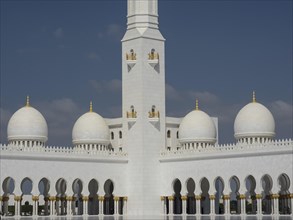 Impressive mosque with white domes and golden decorations under a clear blue sky, beautiful mosque