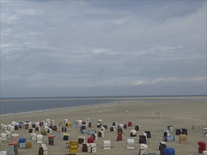 Colourful beach chairs spread out on the wide, sandy beach under a cloudy sky with a view of the
