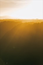 The sun shines through a gap in the clouds over a field with trees. Niederfell, Germany, Europe