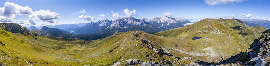 Panorama, mountaineer on a hiking trail between green mountain meadows on a mountain ridge,