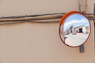 A traffic mirror on the facade of a building reflects a street in the