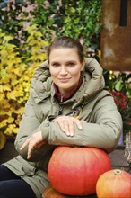 Lovely woman sitting at an autumn fair with her hand on a pumpkin on the table