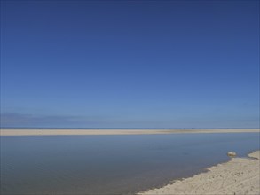 The wide sandy beach meets the calm sea under a clear blue sky, wide sky on the lonely North Sea