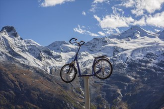 A bicycle is placed high on a post in front of a snowy mountain landscape, snow on high mountains