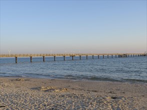 Sandy beach beach with calm sea in the light of the sunset with a long pier in the background,