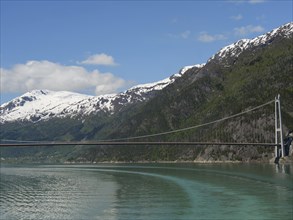 A bridge stretches across the water against a backdrop of snow-capped mountains, bridge in a fjord