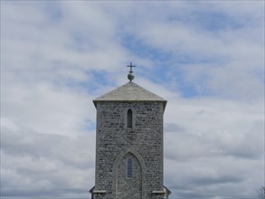 Close-up of a stone church tower under a partly cloudy sky, old stone church and many gravestones
