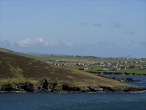 View of a coastal landscape with houses and green hills looking out to sea, green meadows on a deep