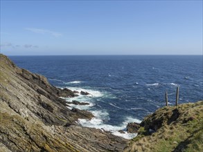 View of a rocky coastline with green grass and blue sea under a clear sky, green meadows on a deep
