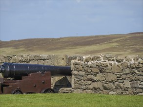 An old gun behind a stone wall overlooking a wide field, old guns on a stone wall by the sea