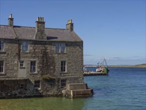 Old stone building on the waterfront with a ship in the background in clear water and a blue sky,