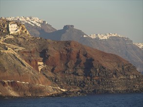 Steep cliffs and white buildings above the sea with a blue sky in the background, rocky island in