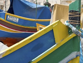 Colourful fishing boats in a Mediterranean harbour with lettering 'ROCKY JOE VALLETTA', many