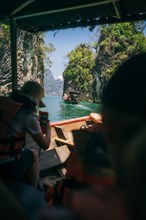 Travellers on a boat experience a sunny boat trip between rock formations. Khao Sok National Park,