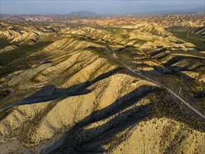 Aerial view of a mountainous desert landscape with shadows and golden lighting at sunset, Dehesas