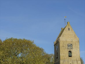 Partial view of a church tower with clock face and trees in front of a blue sky, church tower on