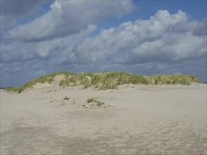 Sand dune landscape under cloudy sky, peaceful natural scenery, lonely beach with dune grass in the