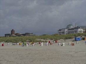 Beach chairs standing on the sandy beach near several buildings under cloudy sky, colourful beach