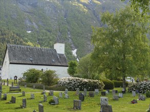 Churchyard with gravestones, flowerbeds and green trees in front of majestic mountains, gravestones