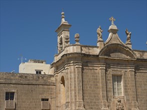 A historic sandstone church with baroque sculptures on the roof and a blue sky, stand-alone church