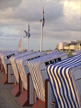 Row of striped beach chairs at sunset by the sea, with buildings and clouds in the background, blue