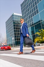 Vertical full length photo with low angle view of an elegant cool businessman crossing the street