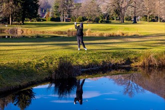 Female Golfer Reflected in a Water Pond and Hitting the Golf Ball on Fairway on Golf Course in a