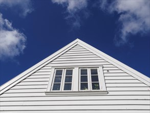 White wooden house with a window in a triangular gable in front of a bright blue sky with few
