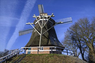 A historic windmill on a hill under a clear blue sky, surrounded by trees, Old windmill with a