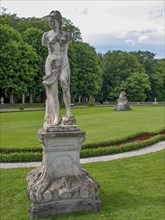 Weathered statue in a well-kept park with green lawns and surrounded by trees, park with green
