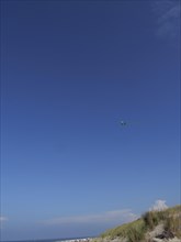 Blue sky with a kite over a beach with dunes, dunes and beach at the sea with dune grass and beach