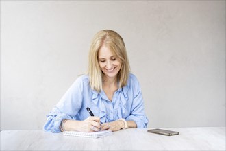 Beautiful mid-adult smiling woman is writing in her notebook