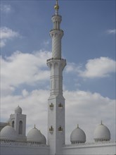 High minaret of a mosque surrounded by white domes and a cloudy sky, large mosque with white domes