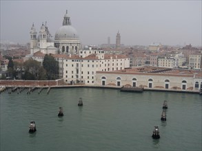 View of Venetian buildings with domes and orange roofs, water and foggy atmosphere, church towers