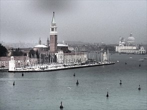 A view of the church and marina of Venice with boats in the water on a cloudy day, church towers