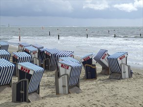 Blue and white beach chairs on a sandy beach with a view of the sea and a cloudy sky, blue and