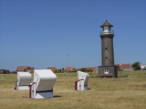 A lighthouse in the middle of a meadow, surrounded by beach chairs and houses under a bright blue