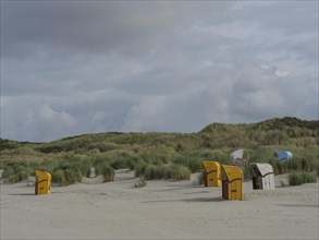 A wide dune landscape with scattered beach chairs under a cloudy sky, colourful beach chairs on the