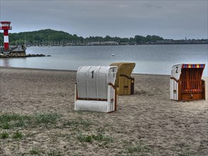 A cloudy day on the beach with a lighthouse in the background and several beach chairs on the sand,