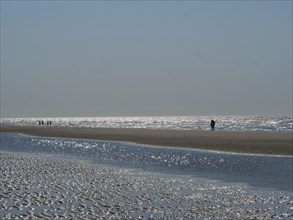 People walking along the beach with reflecting watercourse, glittering sea water at low tide on the